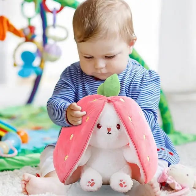 Child playing with a plush toy shaped like a strawberry in a colorful playroom.